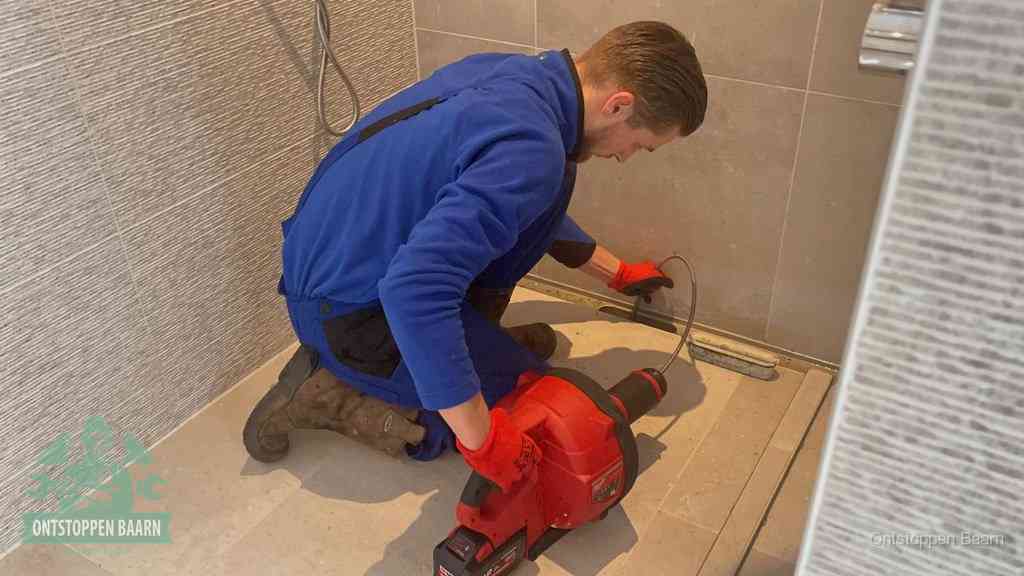 Een monteur ontstopt een langwerpige douchegoot met een elektrische veer, een doucheputje verstopt door haren en zeep in Baarn