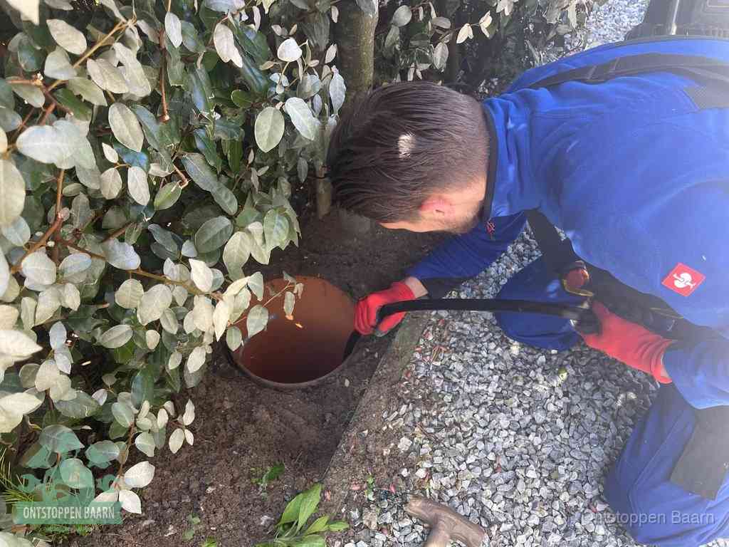 Een monteur voert een slang in een geopende rioolput in de tuin om het hoofdriool te ontstoppen in Baarn