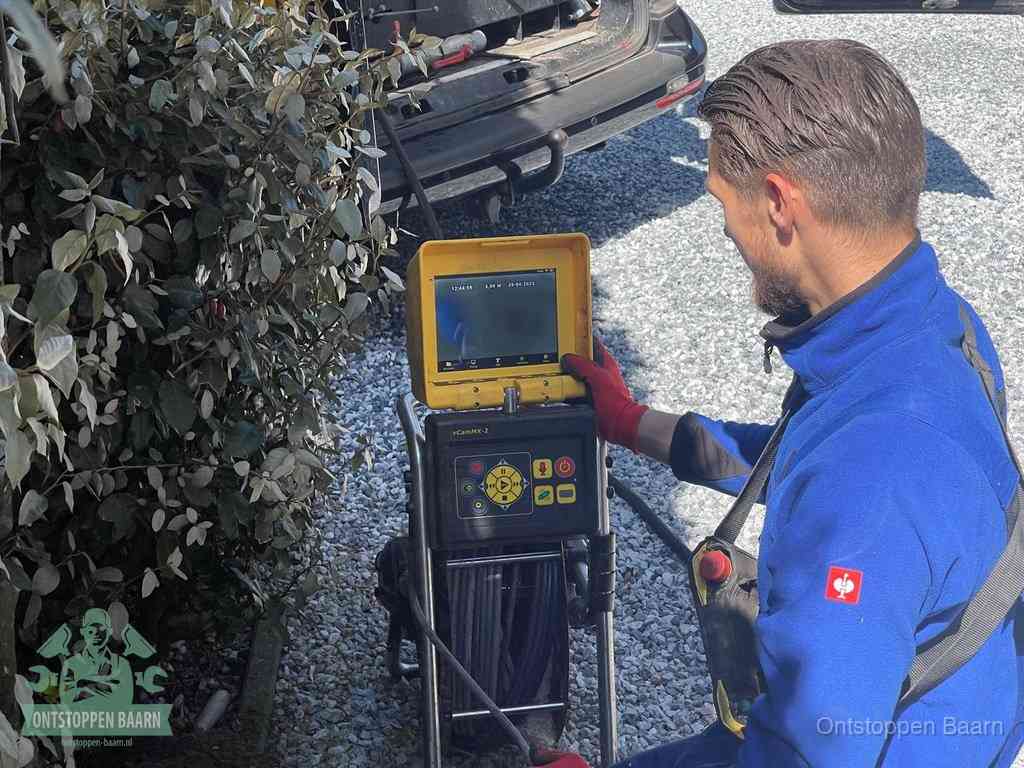 Een monteur bedient een rioolinspectiecamera met monitor en haspel om de verstopping in beeld te brengen in Baarn