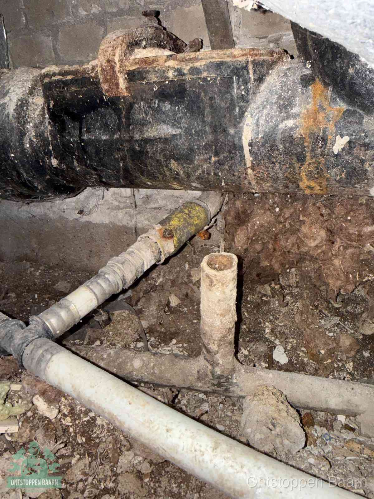 Een oude hoofdrioolbuis met roest- en kalkaanslag in een kruipruimte, oorzaak van terugkerende structurele rioolproblemen in Baarn